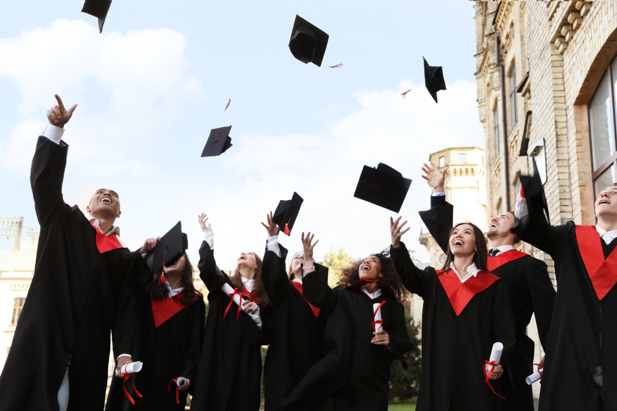 Happy students with diplomas throwing graduation hats in air outdoors