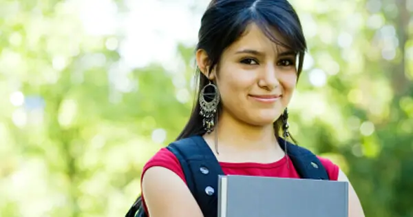 Portrait image of Maria outside, holding her backpack and book